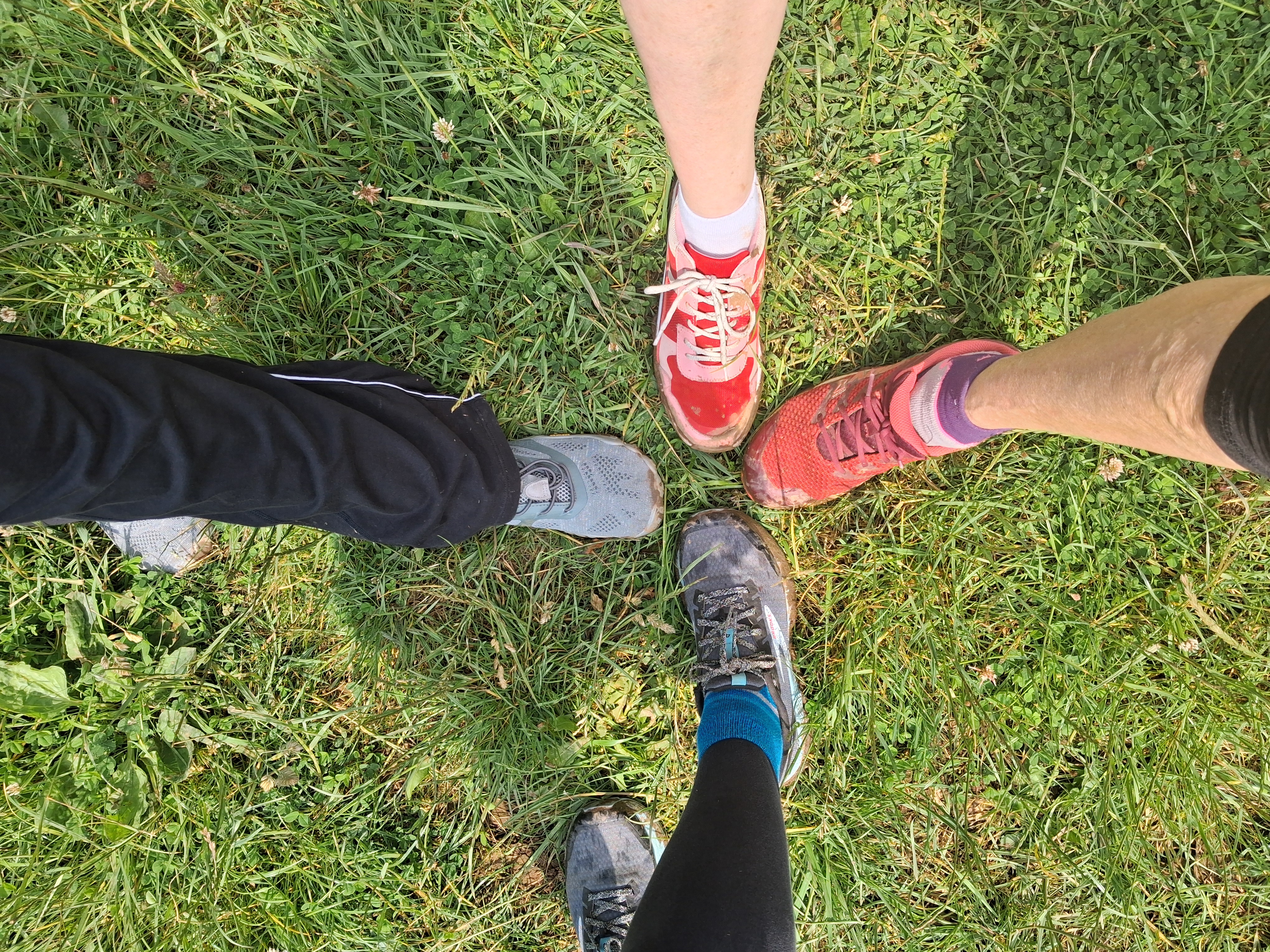 4 individual feet in trainers, touching at the toes and ready to move